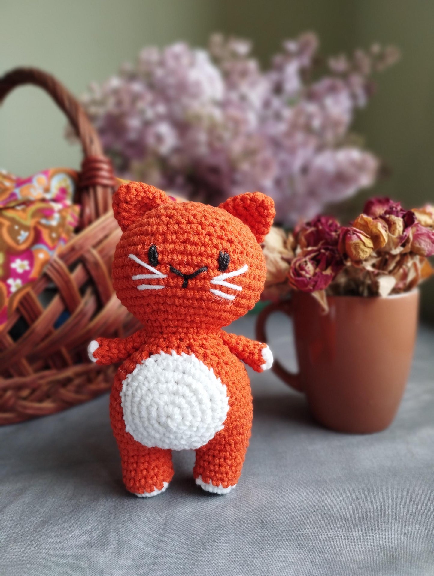 a crocheted cat sitting next to a basket of flowers