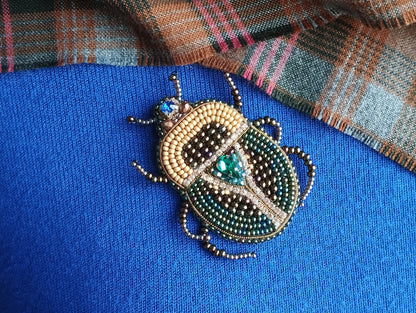A close-up image of a decorative beaded insect, possibly a ladybug or a similar type of insect, on a blue fabric background.