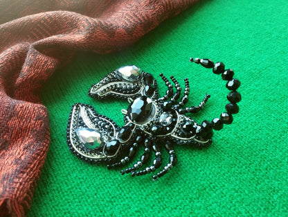 A decorative black and silver piece of jewelry, possibly a brooch or pendant, is displayed on a green surface next to a red and black patterned fabric.