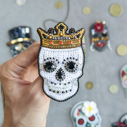 a hand holding a beaded skull with a crown on it