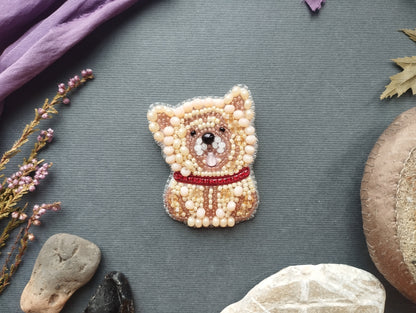 a small, intricately designed beaded dog pin or brooch, surrounded by various natural elements such as rocks, leaves, and flowers, creating a visually appealing and harmonious composition.