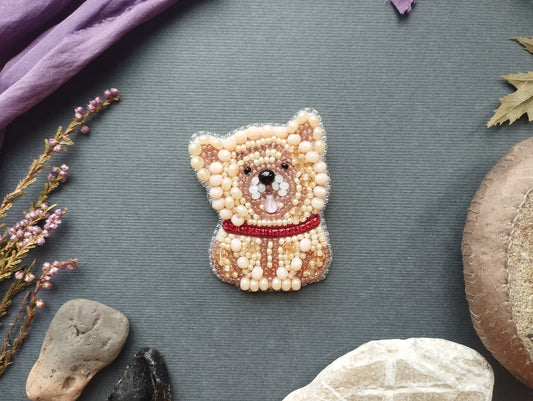 a small, intricately designed beaded dog pin or brooch, surrounded by various natural elements such as rocks, leaves, and flowers, creating a visually appealing and harmonious composition.