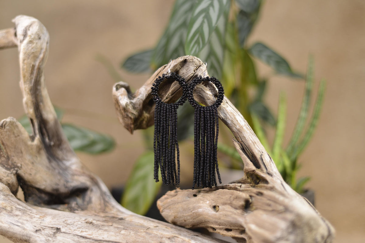 a pair of black beaded earrings sitting on top of a piece of driftwood