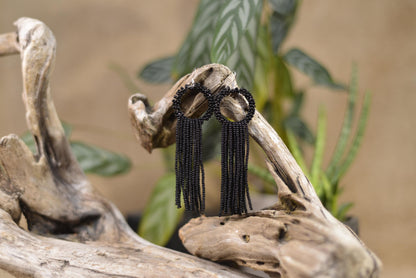 a pair of black beaded earrings sitting on top of a piece of driftwood