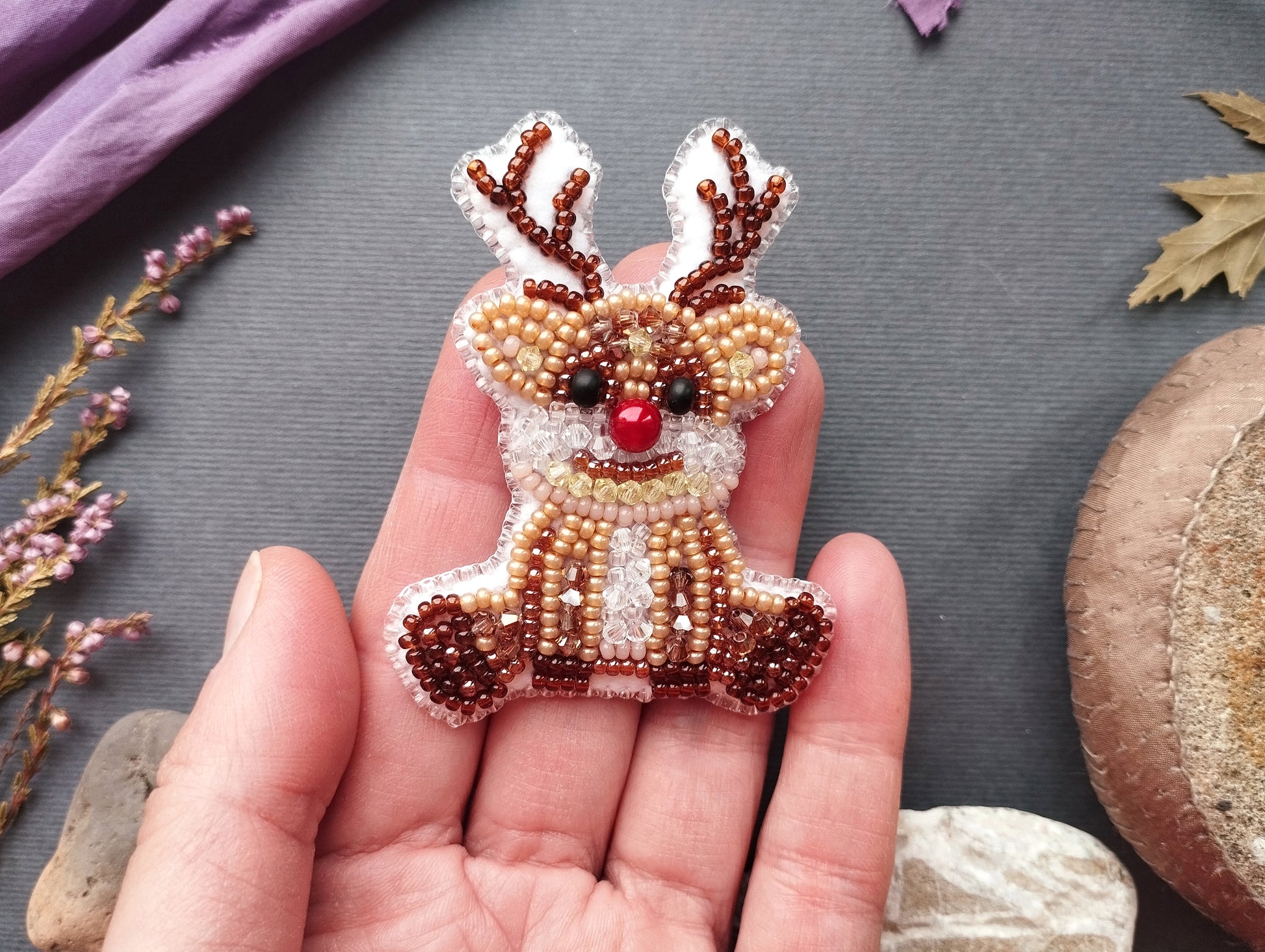 A hand holding a small, beaded reindeer-shaped ornament against a gray background.