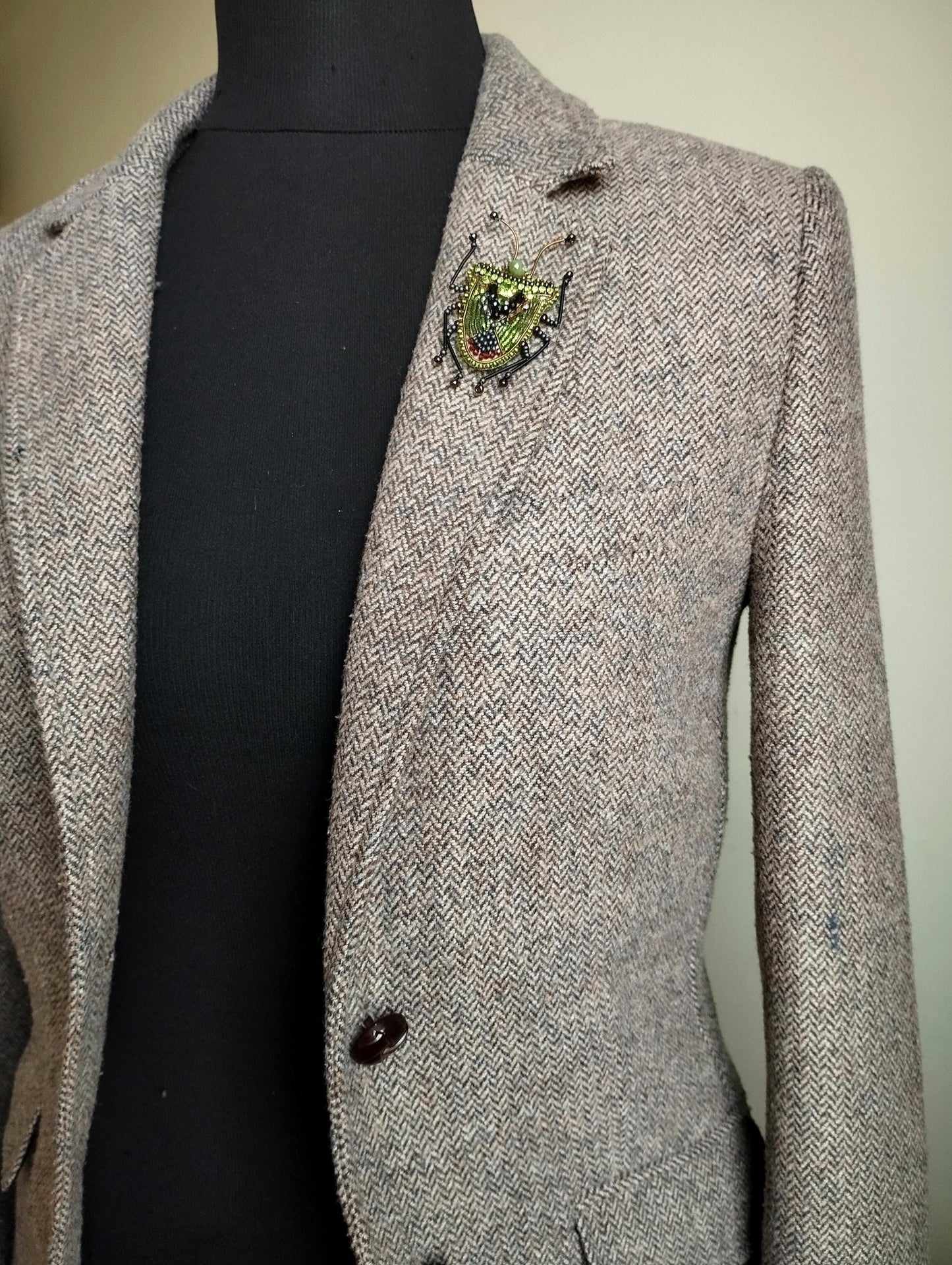 A gray tweed jacket with a decorative brooch on the left breast pocket.