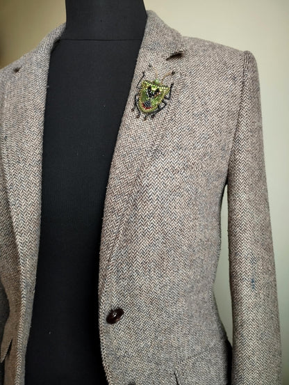 A gray tweed jacket with a decorative brooch on the left breast pocket.