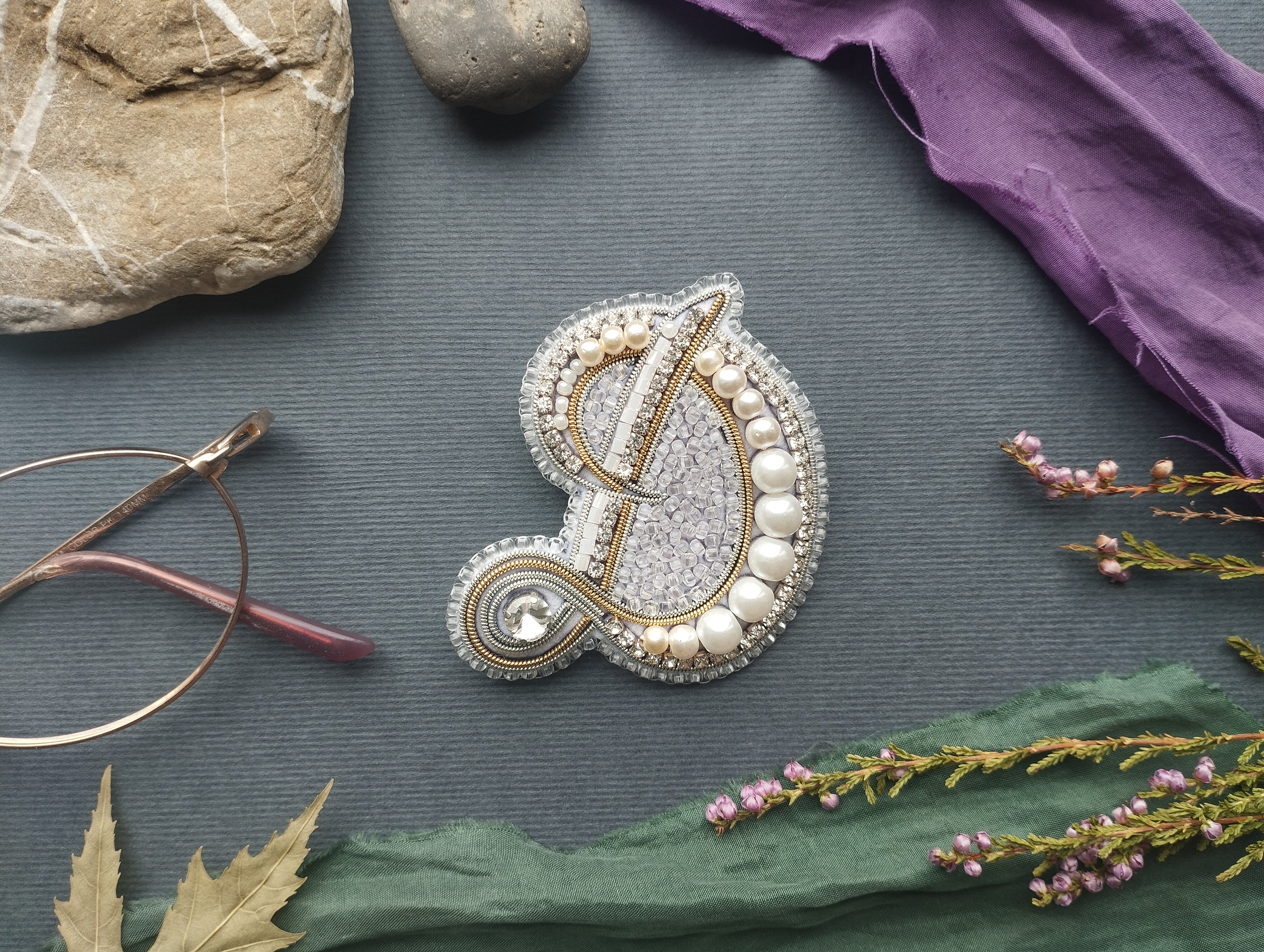 a close-up view of a decorative piece with a letter "D" on it, surrounded by various objects such as a rock, a pair of glasses, and some flowers.