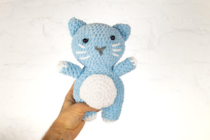 a hand holding a blue and white crocheted cat