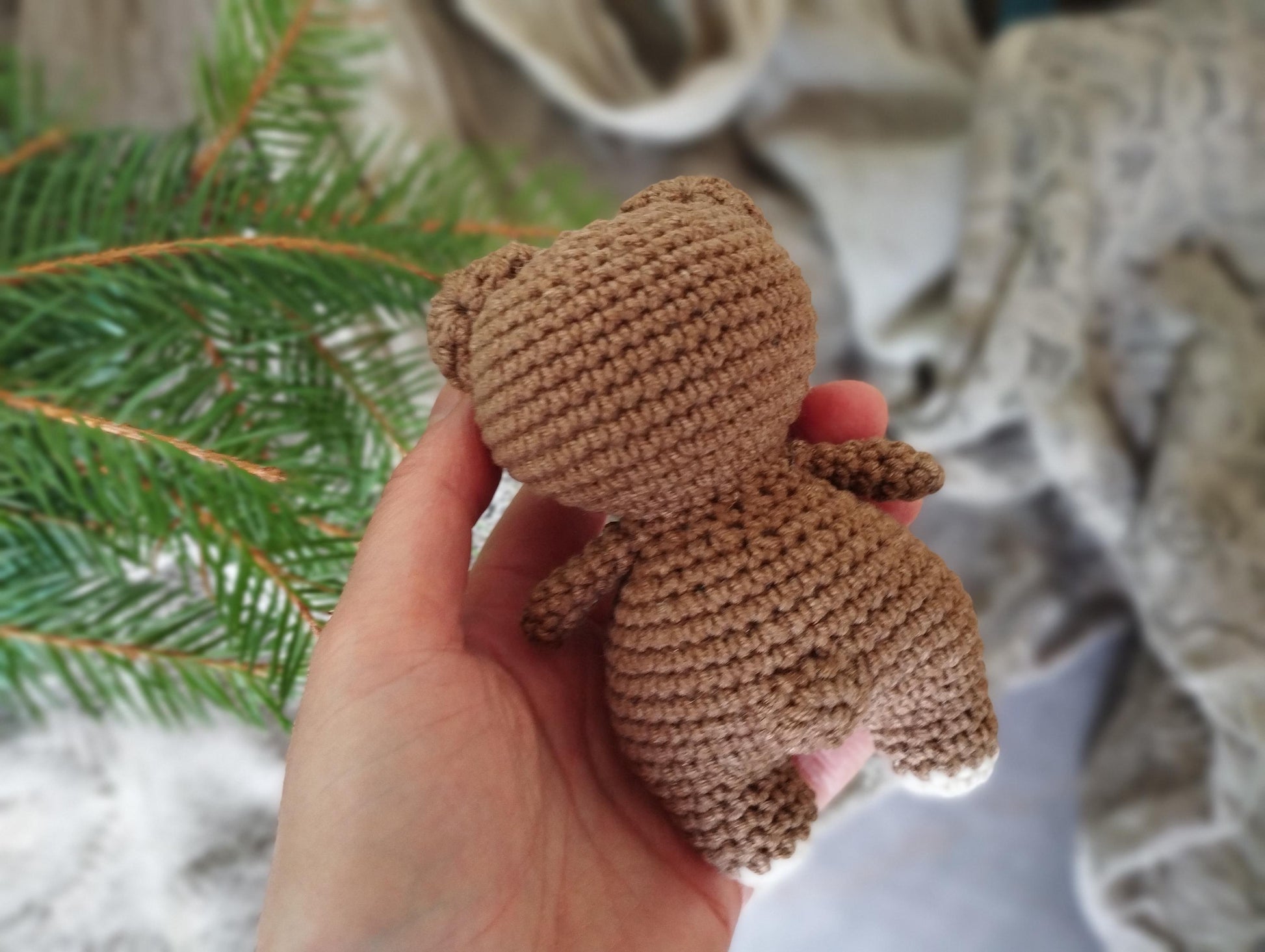 a hand holding a small crocheted teddy bear