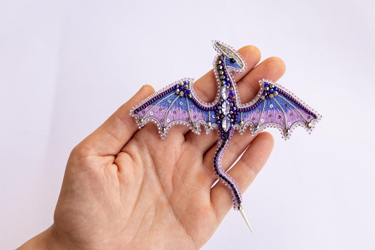 a hand holding a purple and blue dragon brooch