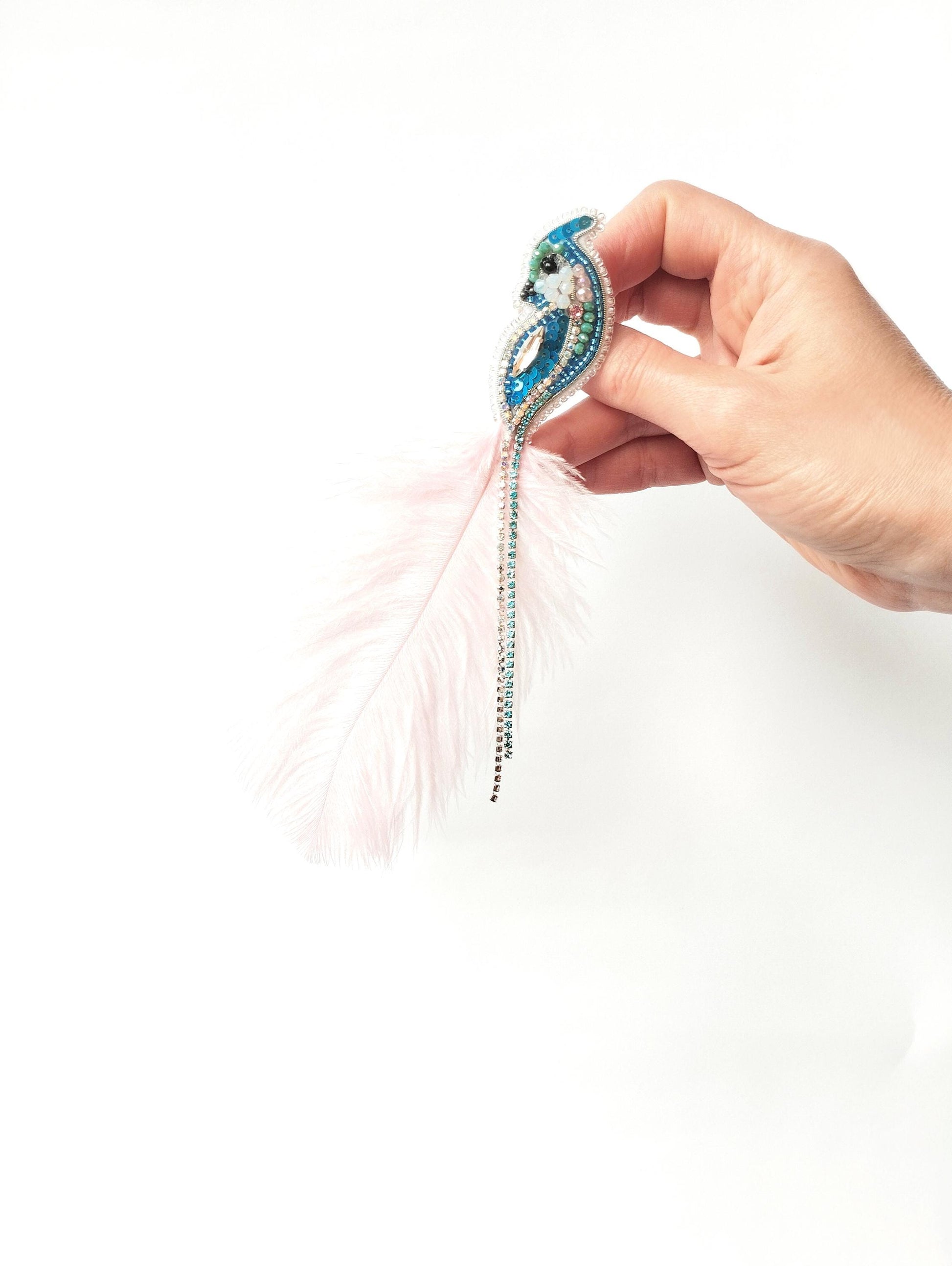 A hand holding a decorative feather earring with a blue and green design.