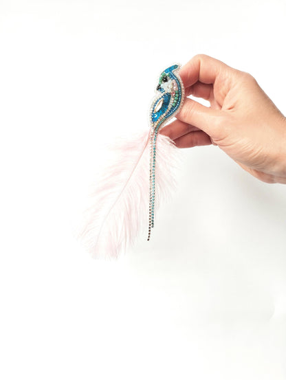 A hand holding a decorative feather earring with a blue and green design.