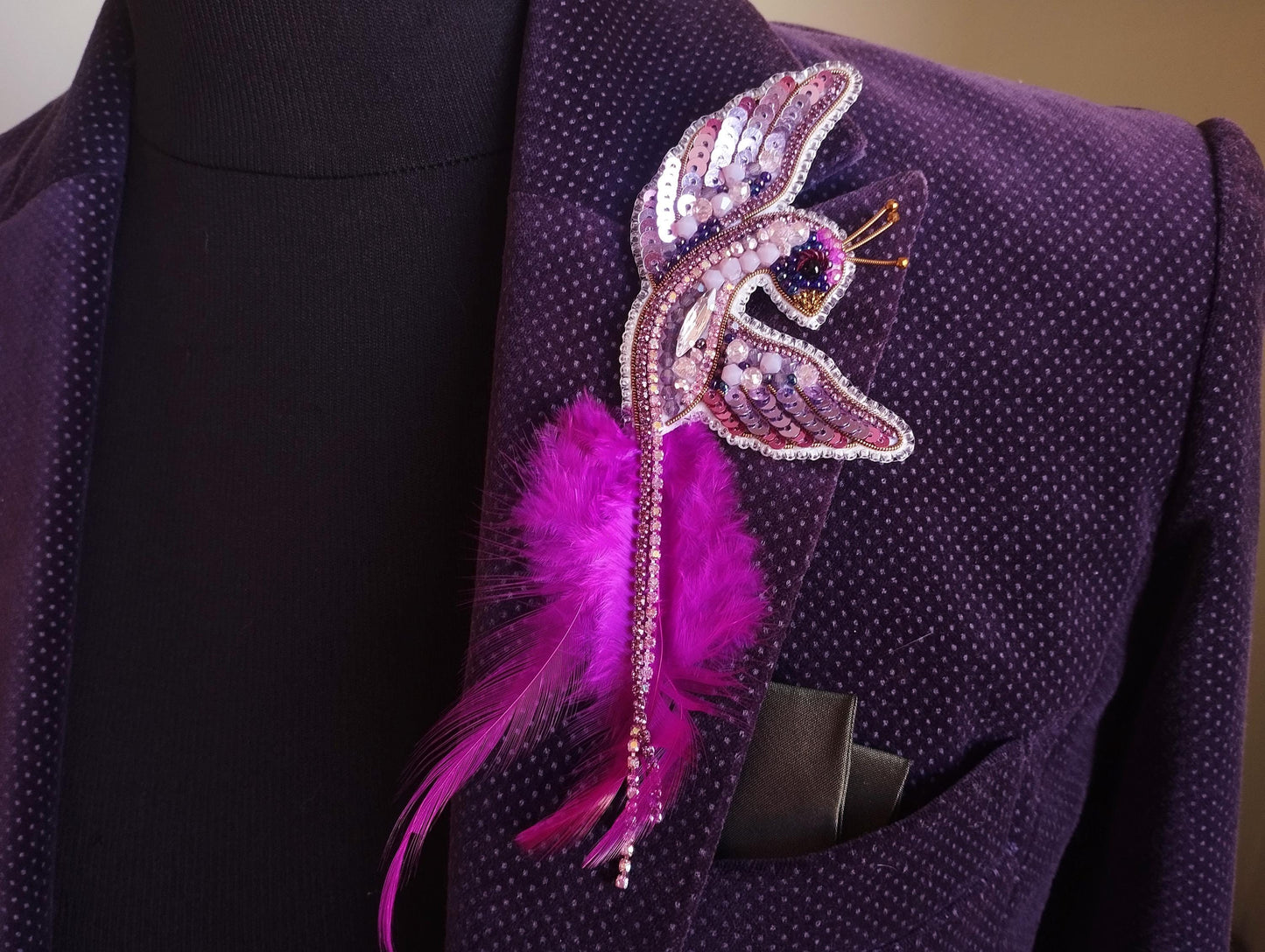 A close-up view of a purple jacket with a decorative pin featuring a pink feather and sequins on the shoulder.