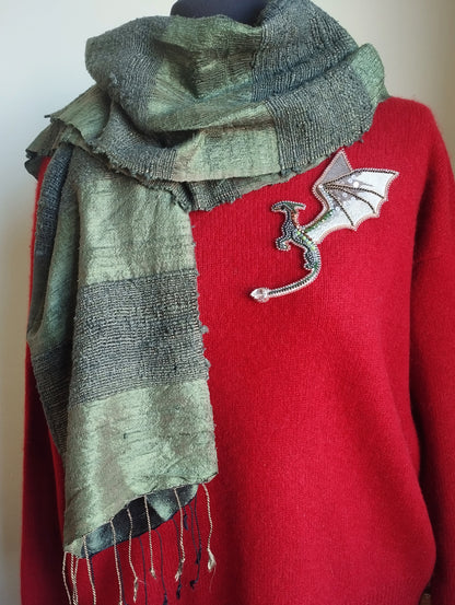 A red sweater with a green and gray scarf draped over it, and a small dragon embroidered on the front.
