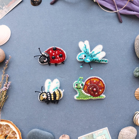 four beaded insects - a ladybug, a dragonfly, a bee, and a snail - arranged on a blue background.