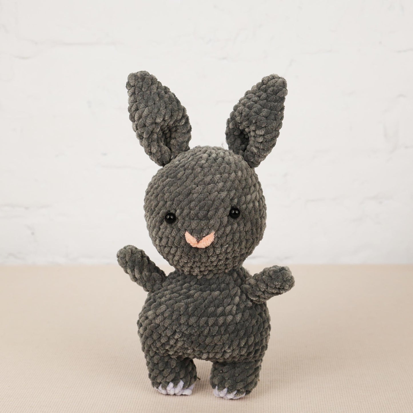 a gray knitted toy rabbit standing on its hind legs