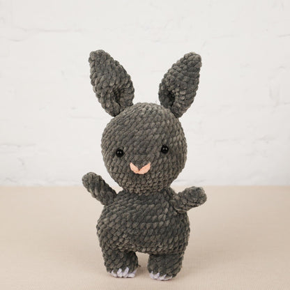 a gray knitted toy rabbit standing on its hind legs