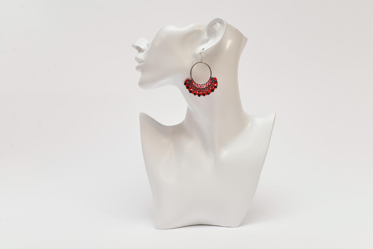 A white bust form is displayed against a plain white background, with a pair of red earrings hanging from the ear.