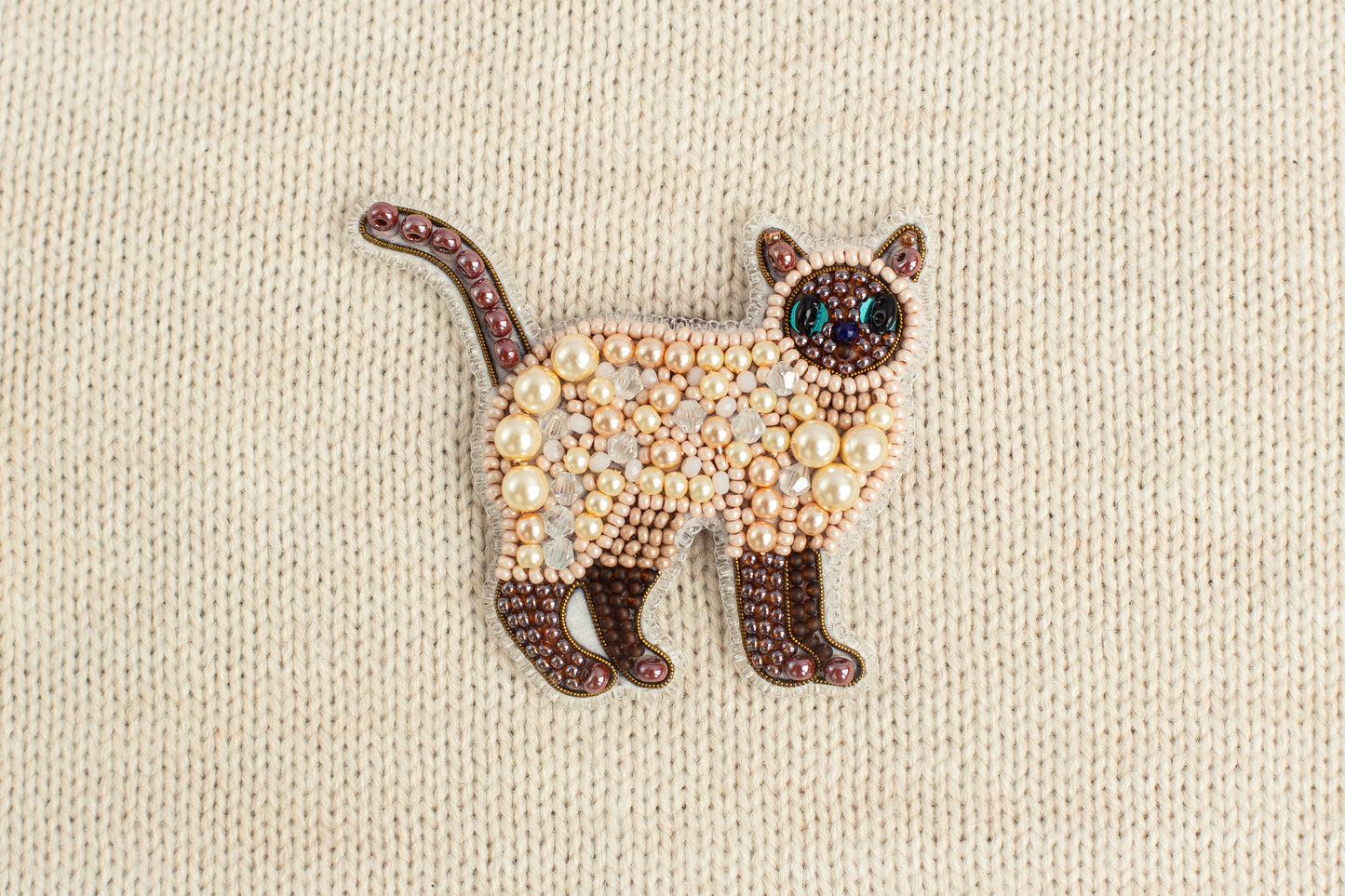A decorative cat brooch made of beads and pearls, featuring a brown and white color scheme.