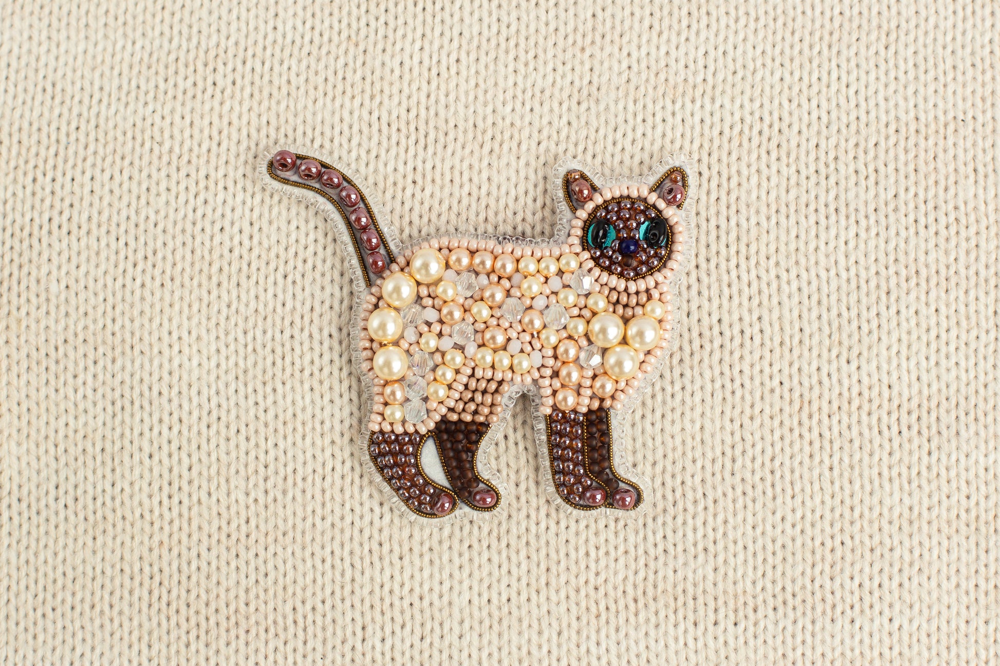 A decorative cat brooch made of beads and pearls, featuring a brown and white color scheme.