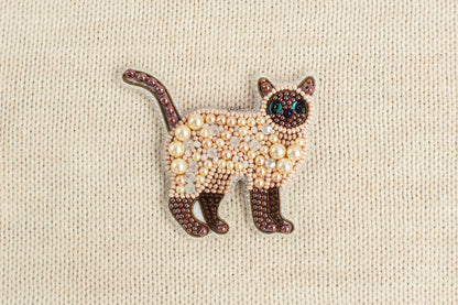 A decorative cat brooch made of beads and pearls, featuring a brown and white color scheme.