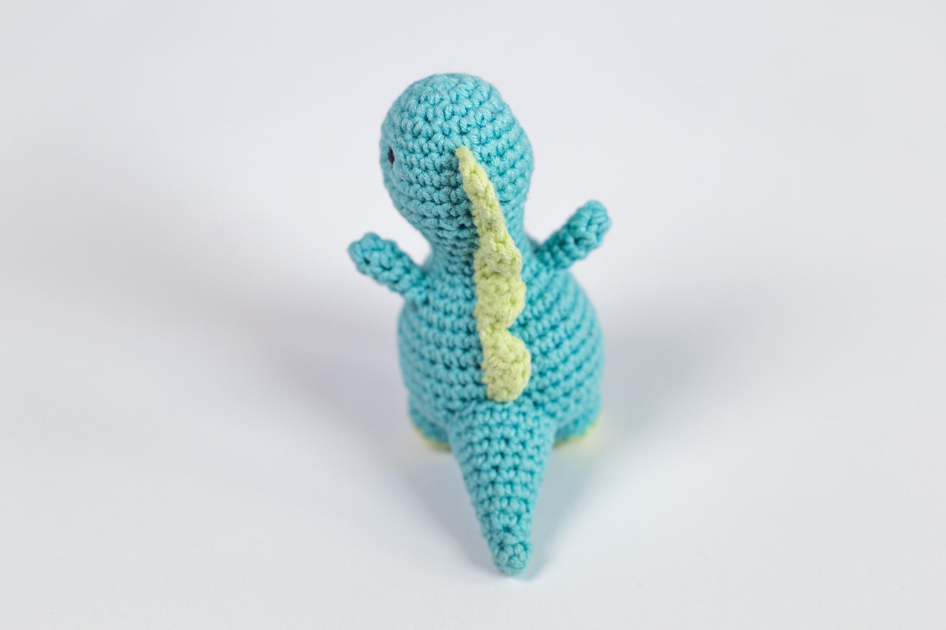 a crocheted toy of a blue dinosaur with a yellow tail