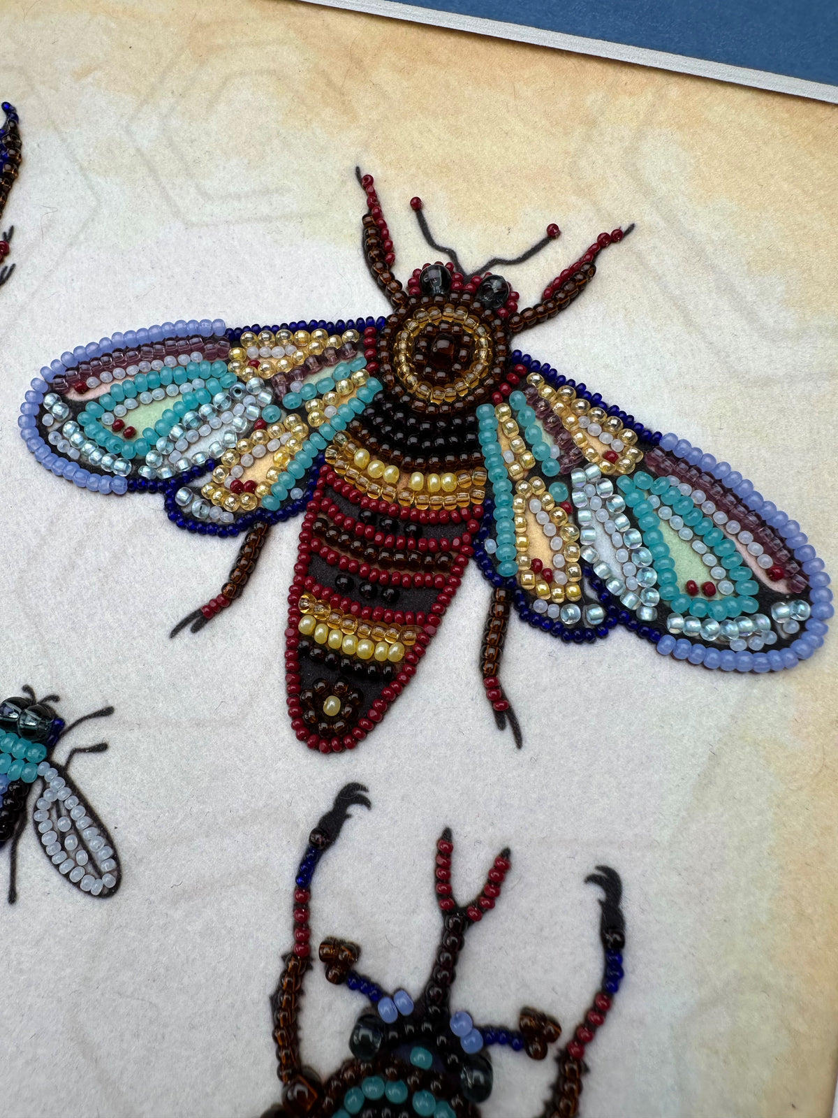 a detailed and colorful beaded insect, possibly a bee or a dragonfly, crafted from numerous small beads in various colors and patterns.