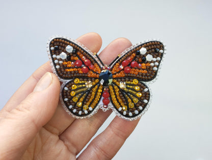 a hand is holding a beaded butterfly brooch