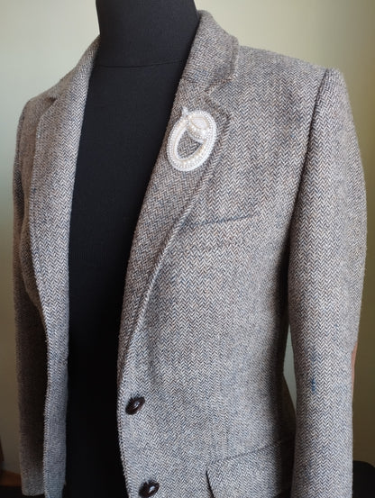 A gray tweed blazer with a white brooch on the lapel, displayed on a mannequin.