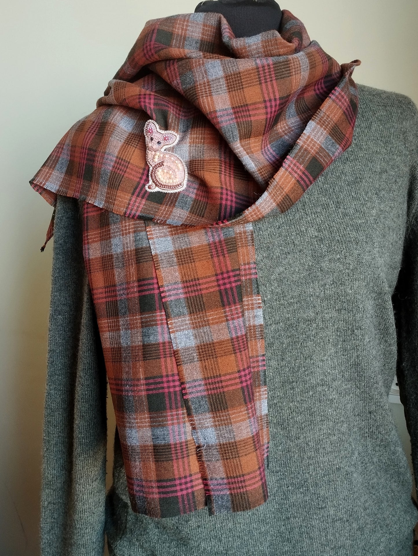 A mannequin wearing a gray sweater and a plaid scarf with a small embroidered cat design.
