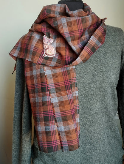 A mannequin wearing a gray sweater and a plaid scarf with a small embroidered cat design.