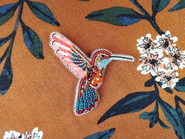 a colorful bird brooch sitting on top of a flowery fabric