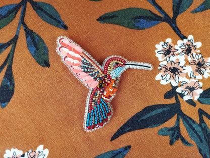 a colorful bird brooch sitting on top of a flowery fabric