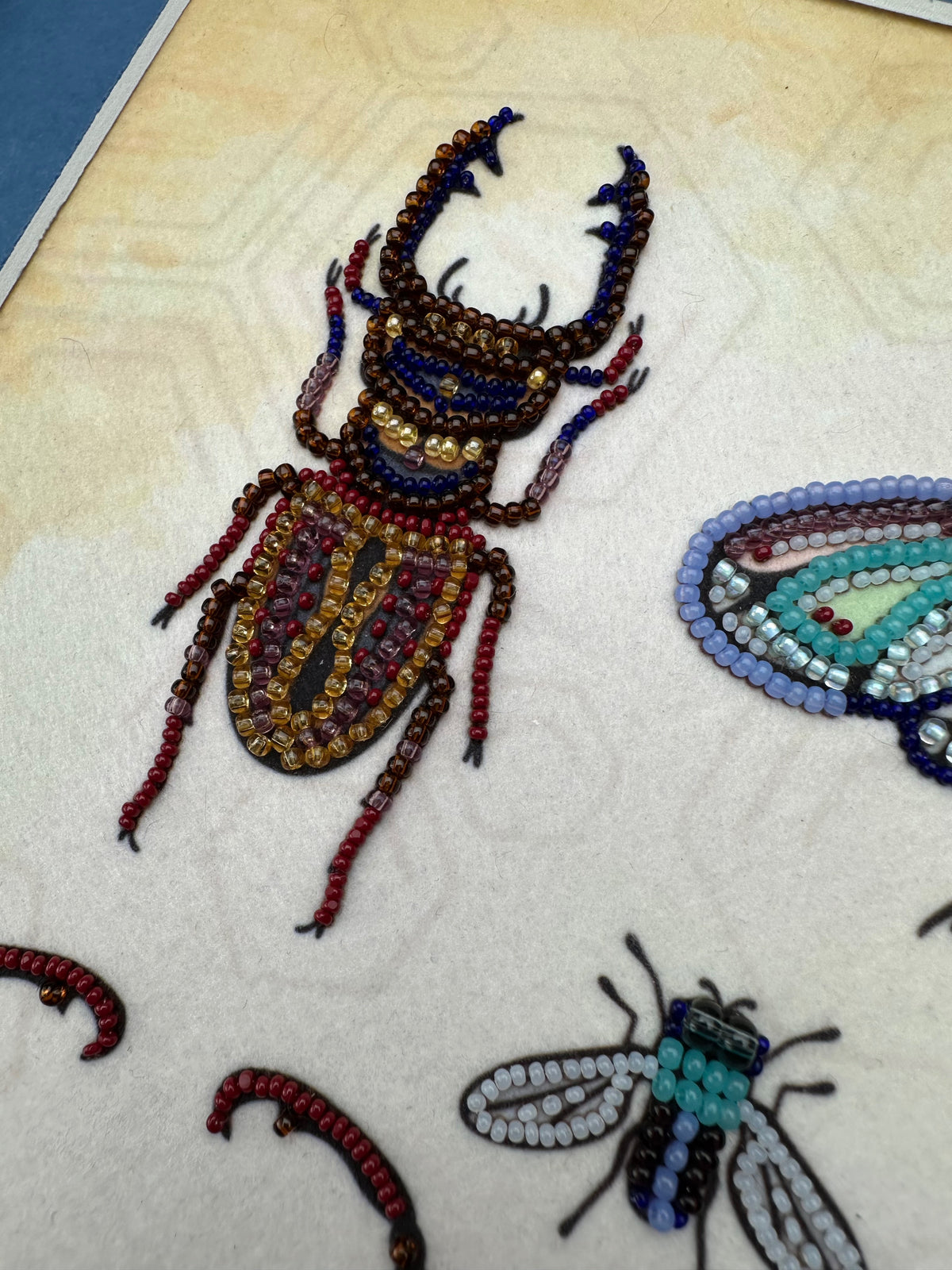a close-up view of a detailed embroidered design of a large insect, possibly a beetle, with intricate beadwork.