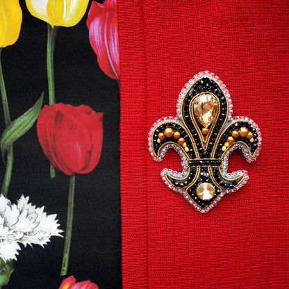 a close-up of a decorative brooch with a black and gold design, placed on a red fabric.