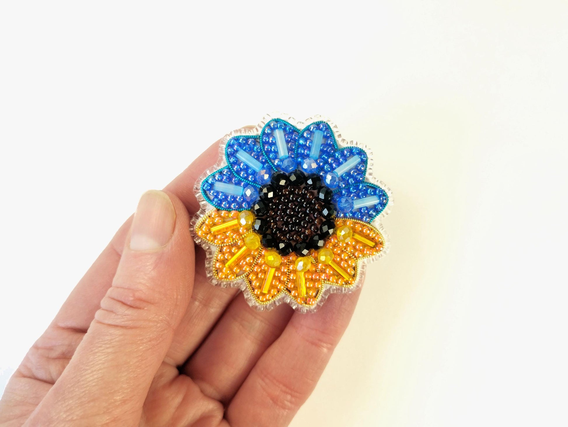 A hand holding a colorful, beaded flower-shaped object against a white background.