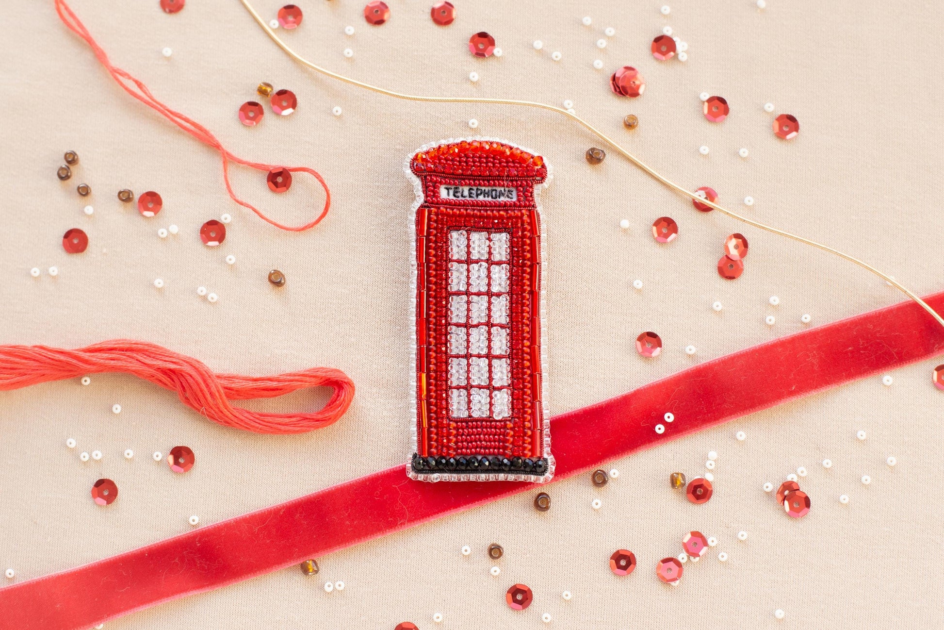 a red telephone booth, surrounded by various craft materials such as beads, string, and a ribbon.