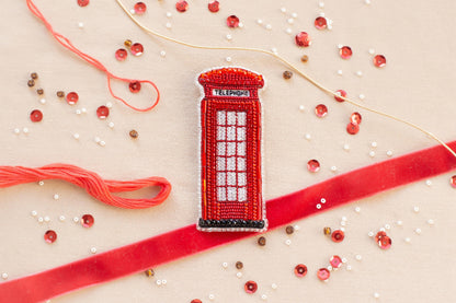 a red telephone booth, surrounded by various craft materials such as beads, string, and a ribbon.