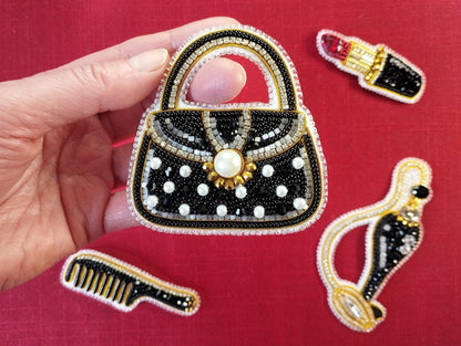A hand holding a handbag embroidered with black and white polka dots, surrounded by other handbag-shaped embroidery pieces on a red background.