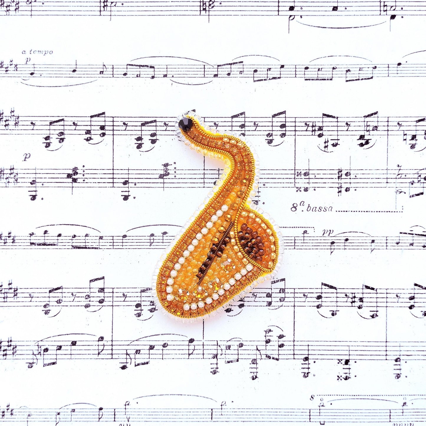 A golden, beaded saxophone rests on top of sheet music, creating a visually striking composition.