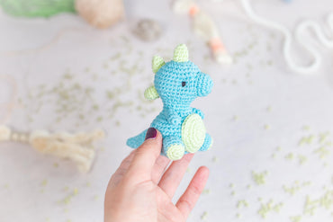 a hand holding a small crocheted blue and green stuffed animal