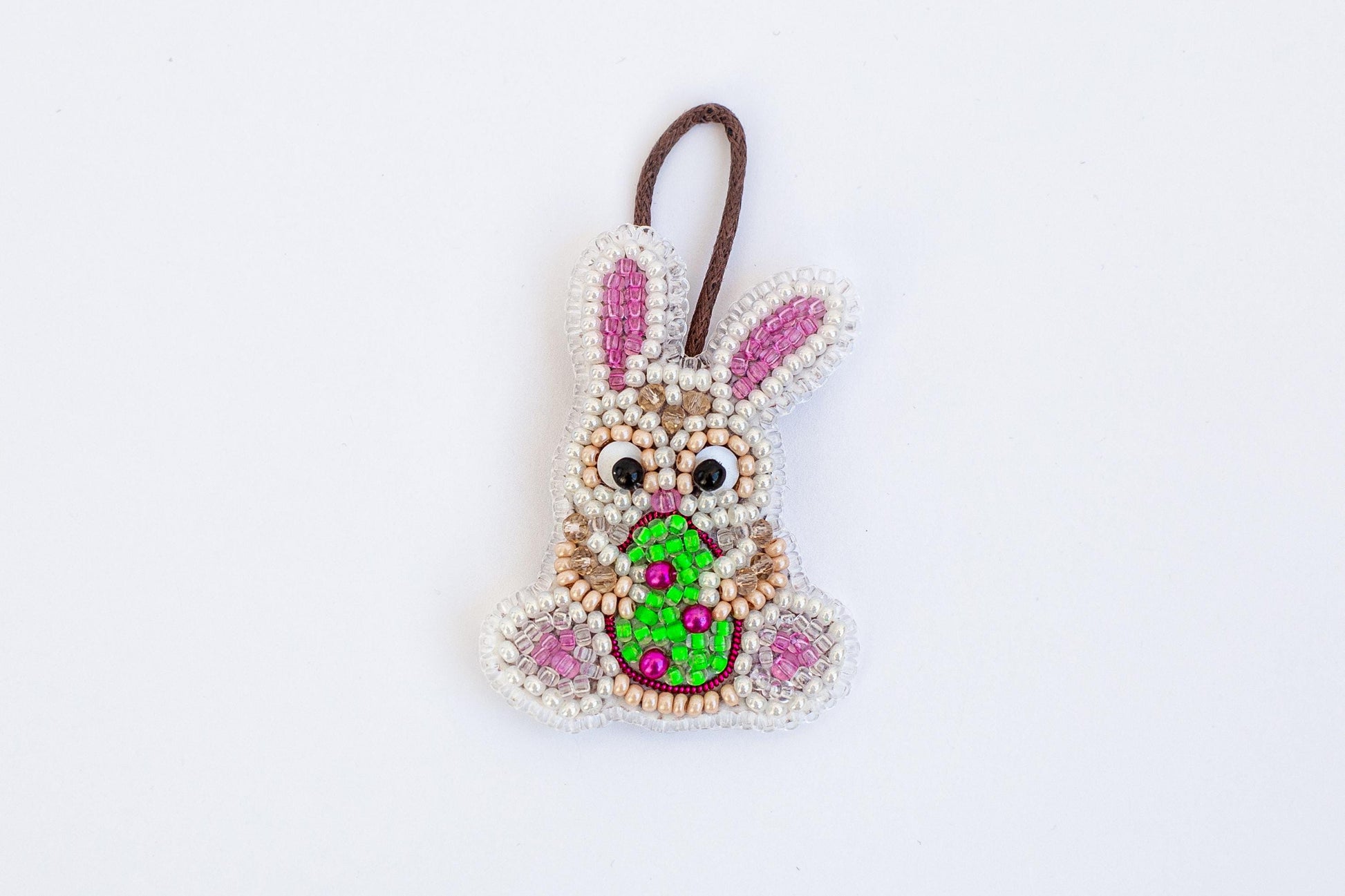 A beaded Easter bunny ornament with a green egg in its mouth, hanging against a white background.
