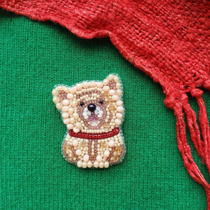 A beaded embroidered dog pin is placed on a green fabric, with a red fabric draped over the right side of the image.