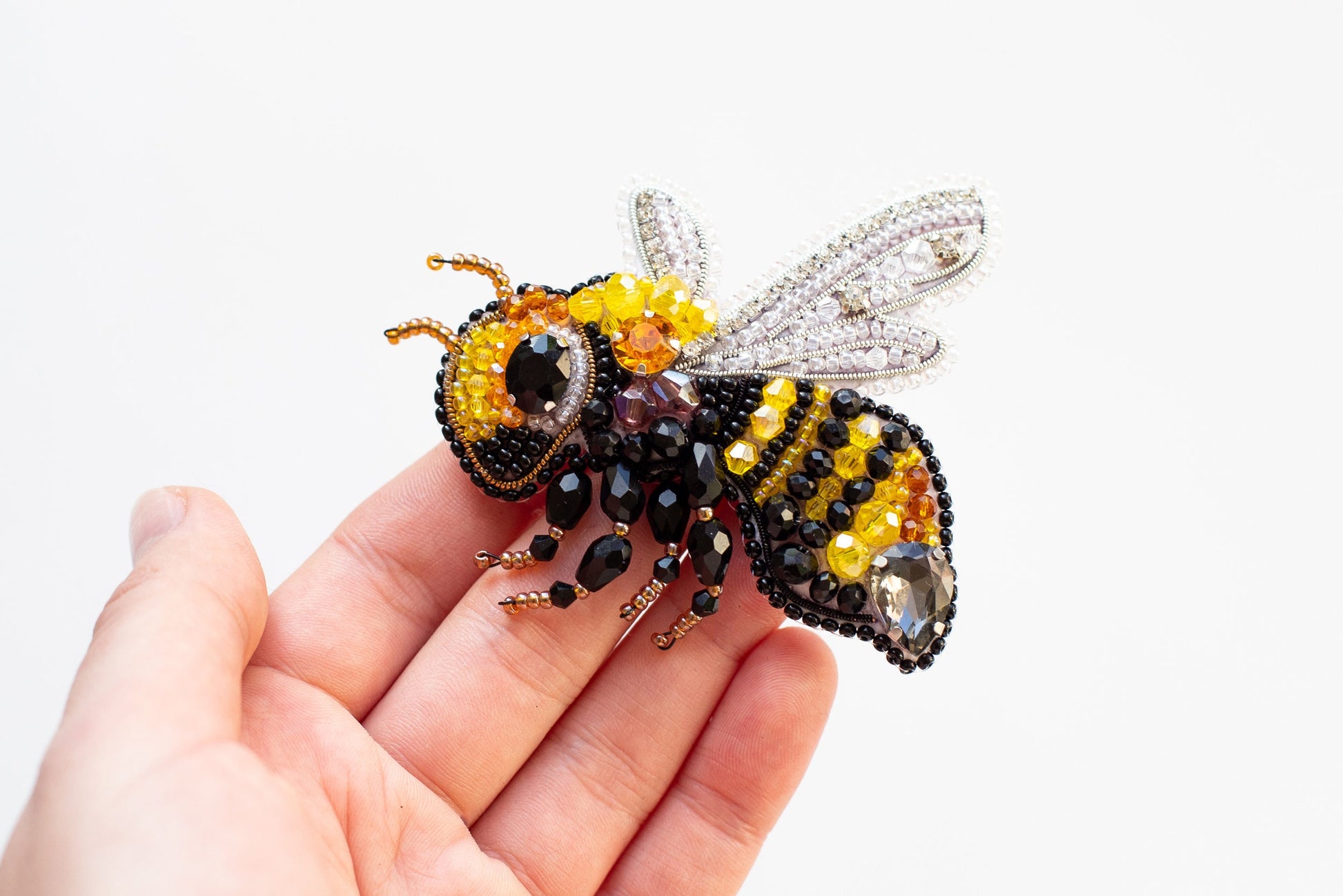 a hand holding a beaded bee on a white background