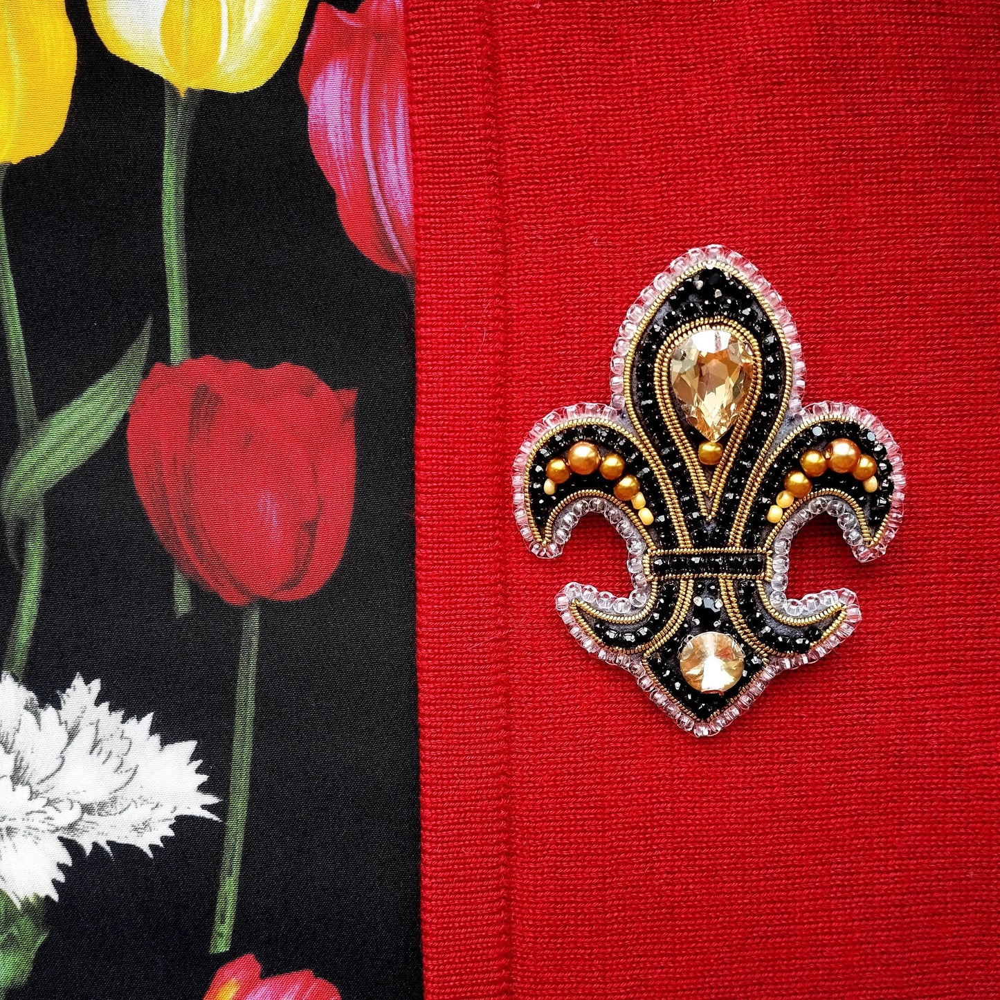 a close-up of a decorative brooch with a black and gold design, placed on a red fabric.