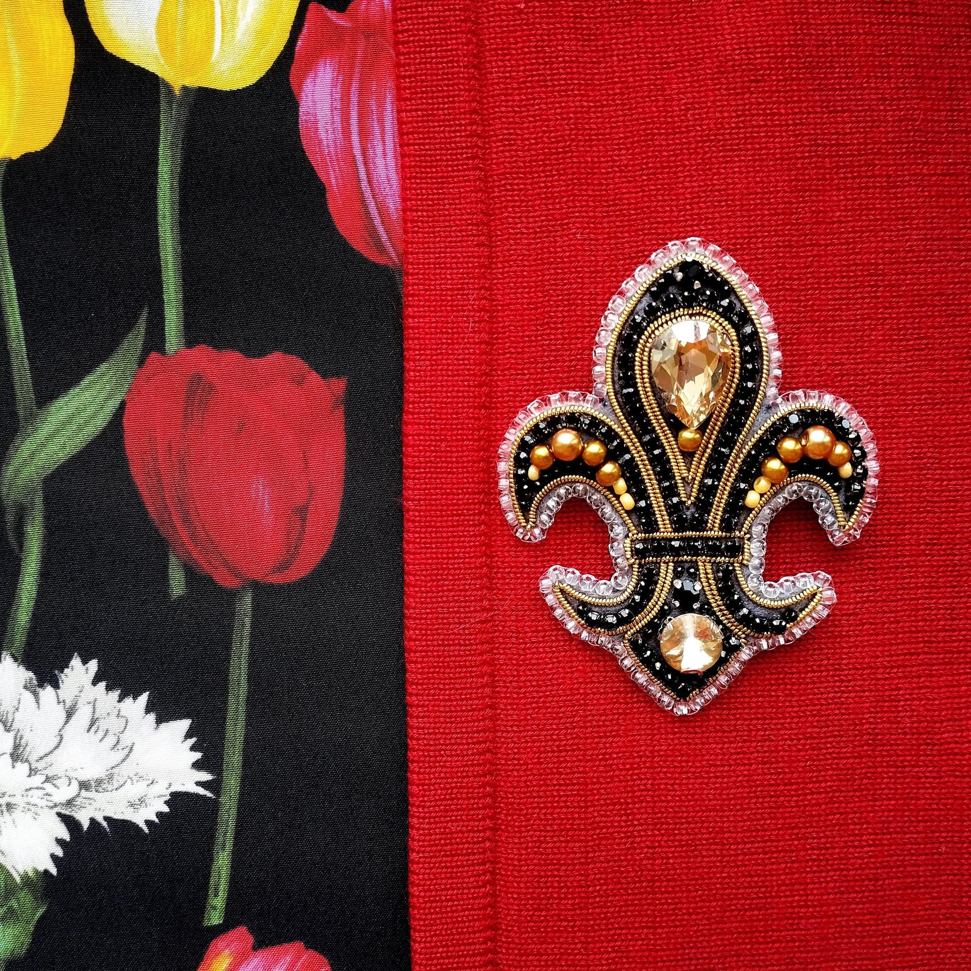 a close-up of a decorative brooch with a black and gold design, placed on a red fabric.