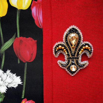 a close-up of a decorative brooch with a black and gold design, placed on a red fabric.