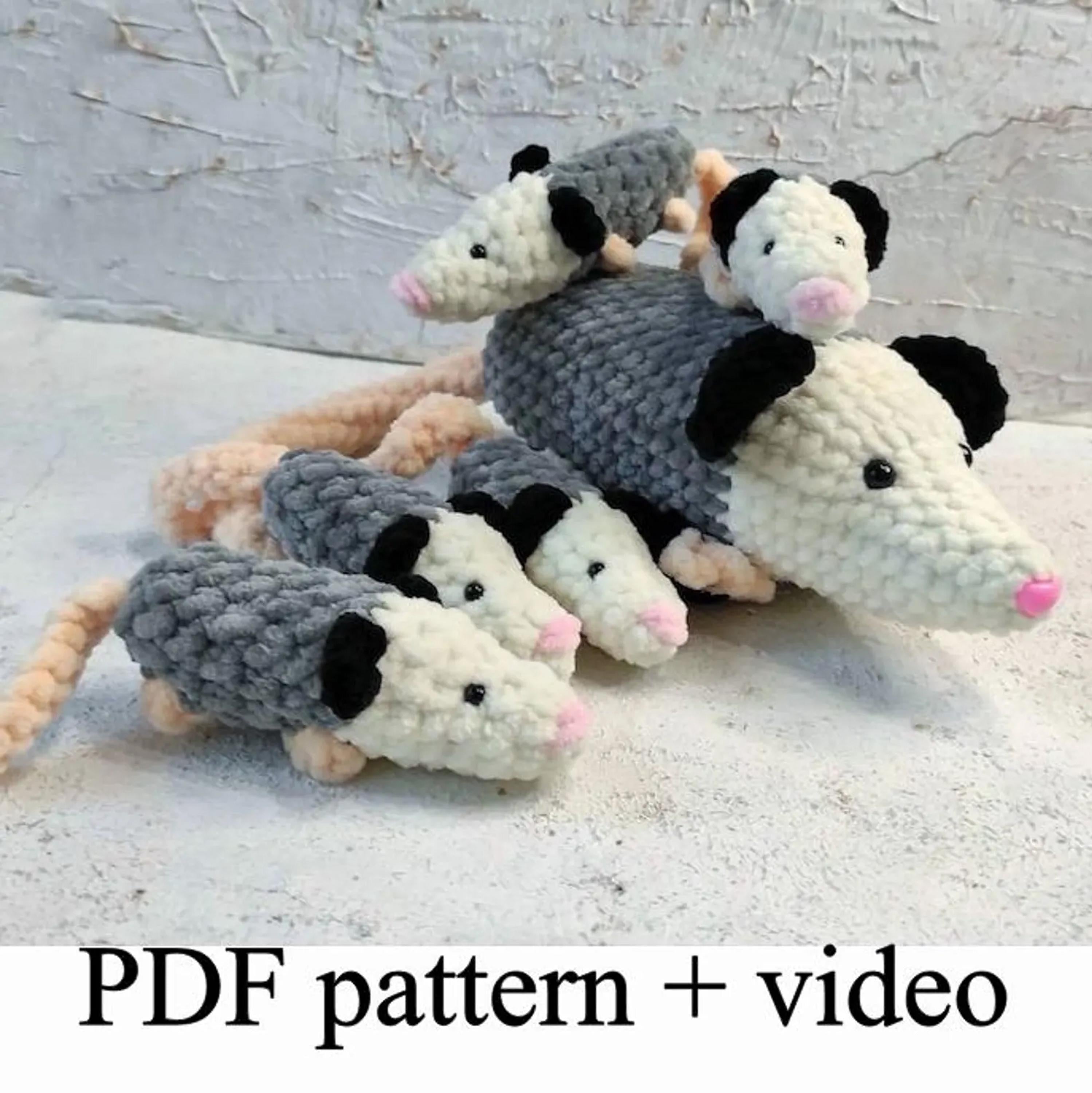 A group of crocheted opossum toys, including a mother opossum and her three offspring, arranged on a white surface.
