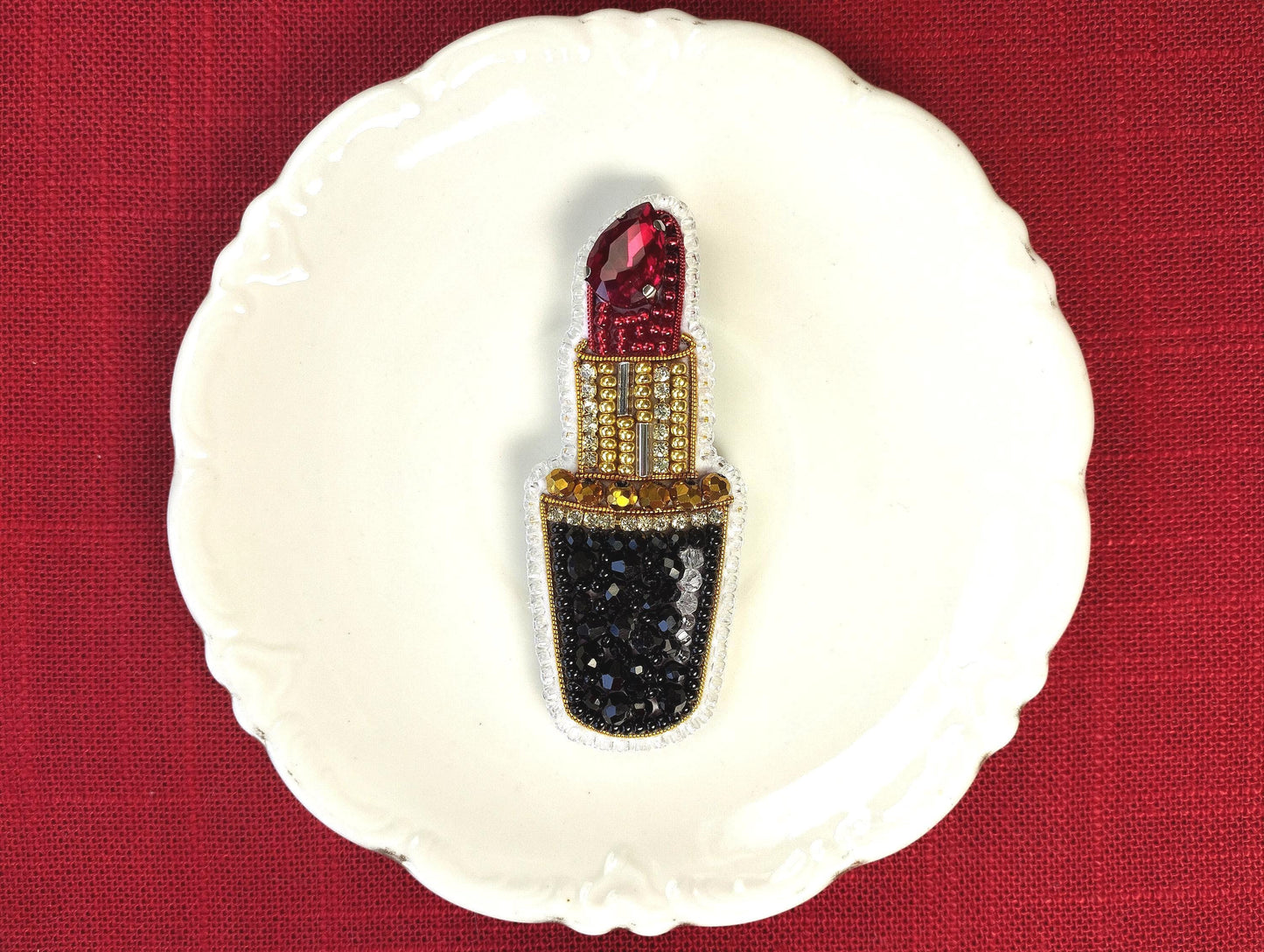 A white plate with a decorative piece featuring a red and gold lipstick design.